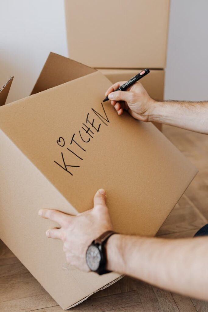 pexels photo 4506265 Crop unrecognizable male using black marker to write on carton container word kitchen and draw heart to identify box with packed kitchenware during relocation