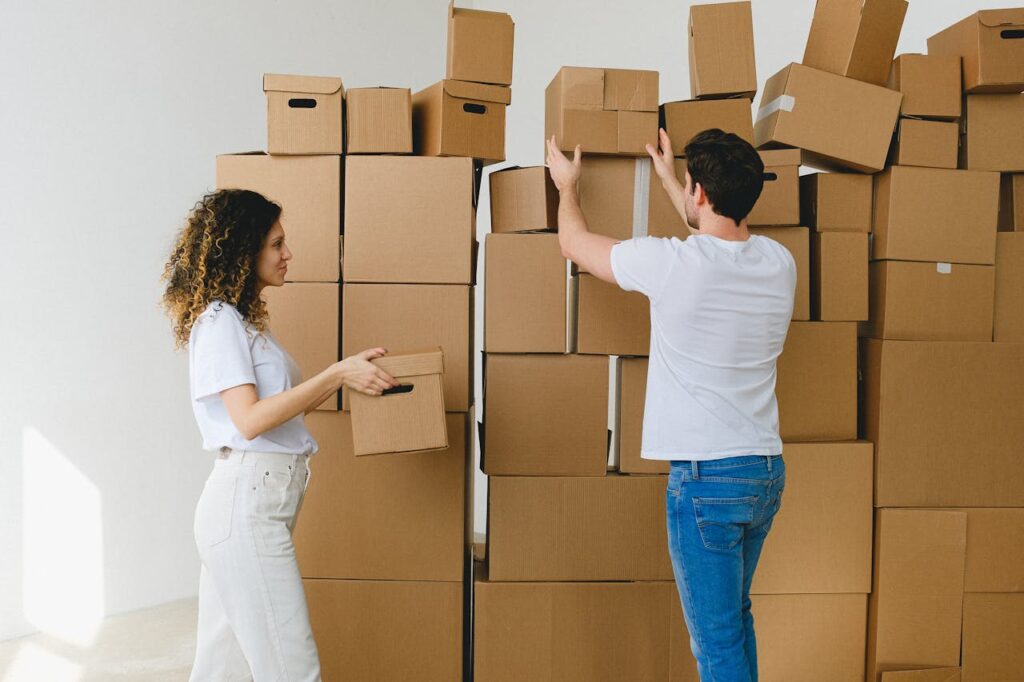pexels photo 7203783 Young man and woman in casual clothes carrying and arranging cardboard boxes after receiving parcels during relocation into new light apartment